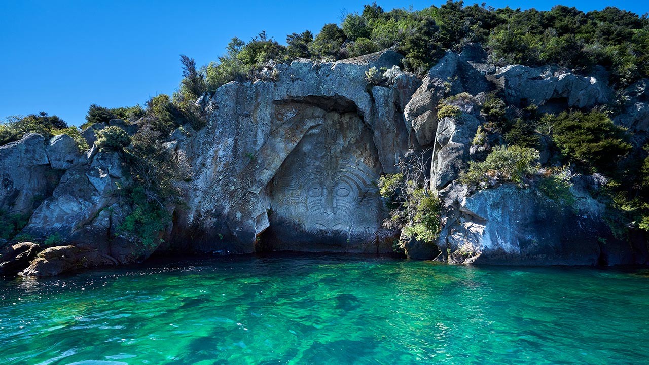A Maori carving carved into the side of a cliff beside the water