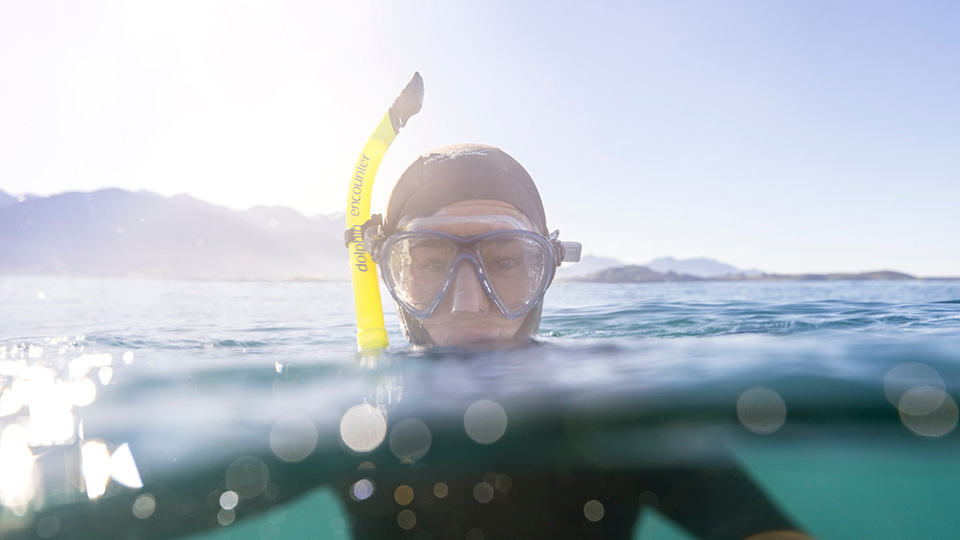 A person, in a full wetsuit with a yellow snorkel, with their head above the water